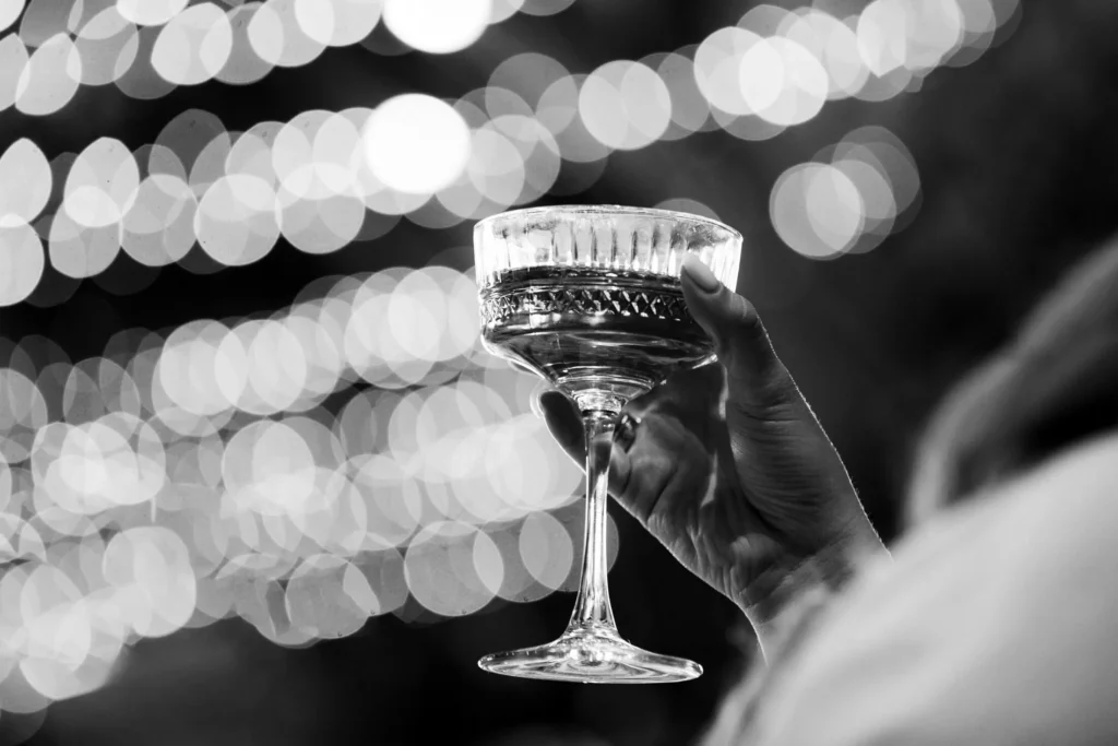 A hand holding a cocktail glass at an evening party with string lights behind